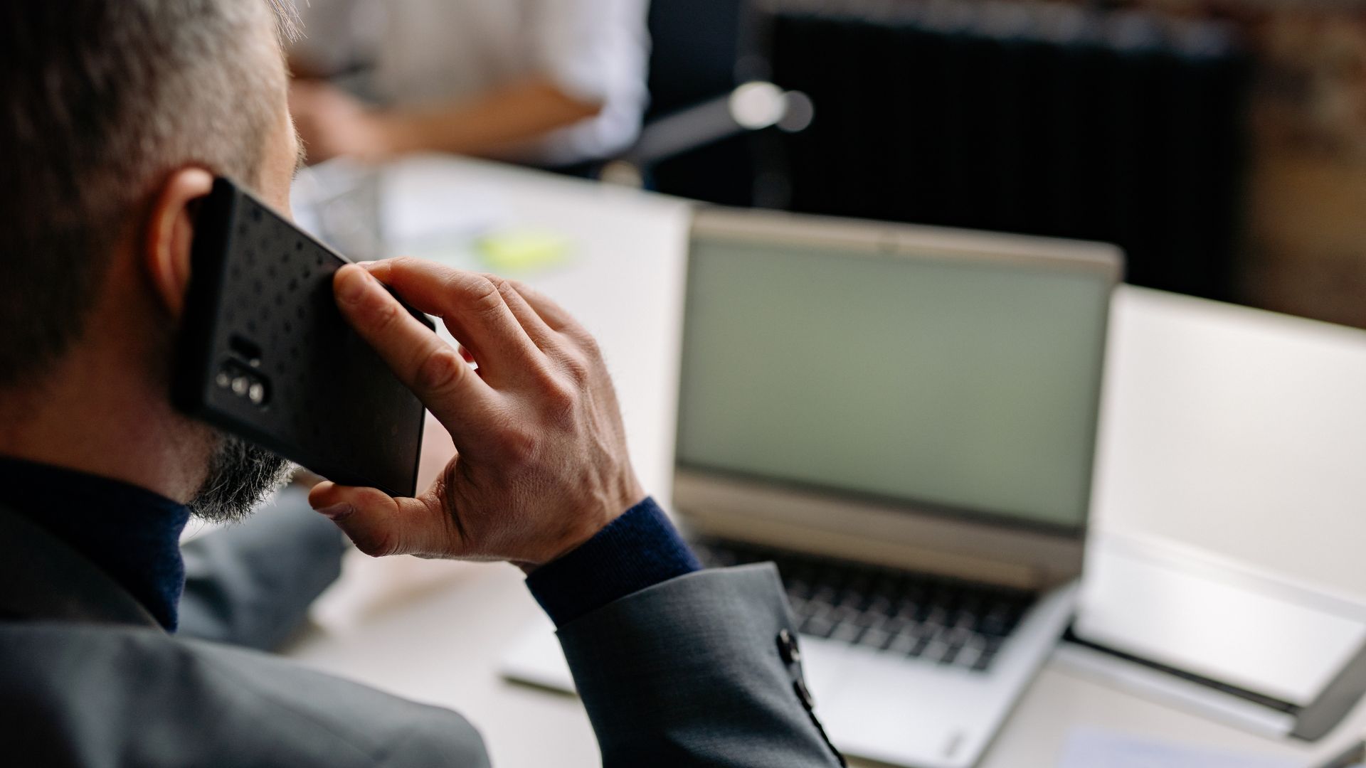 Un uomo al telefono accanto al portatile, mentre lavora in ufficio