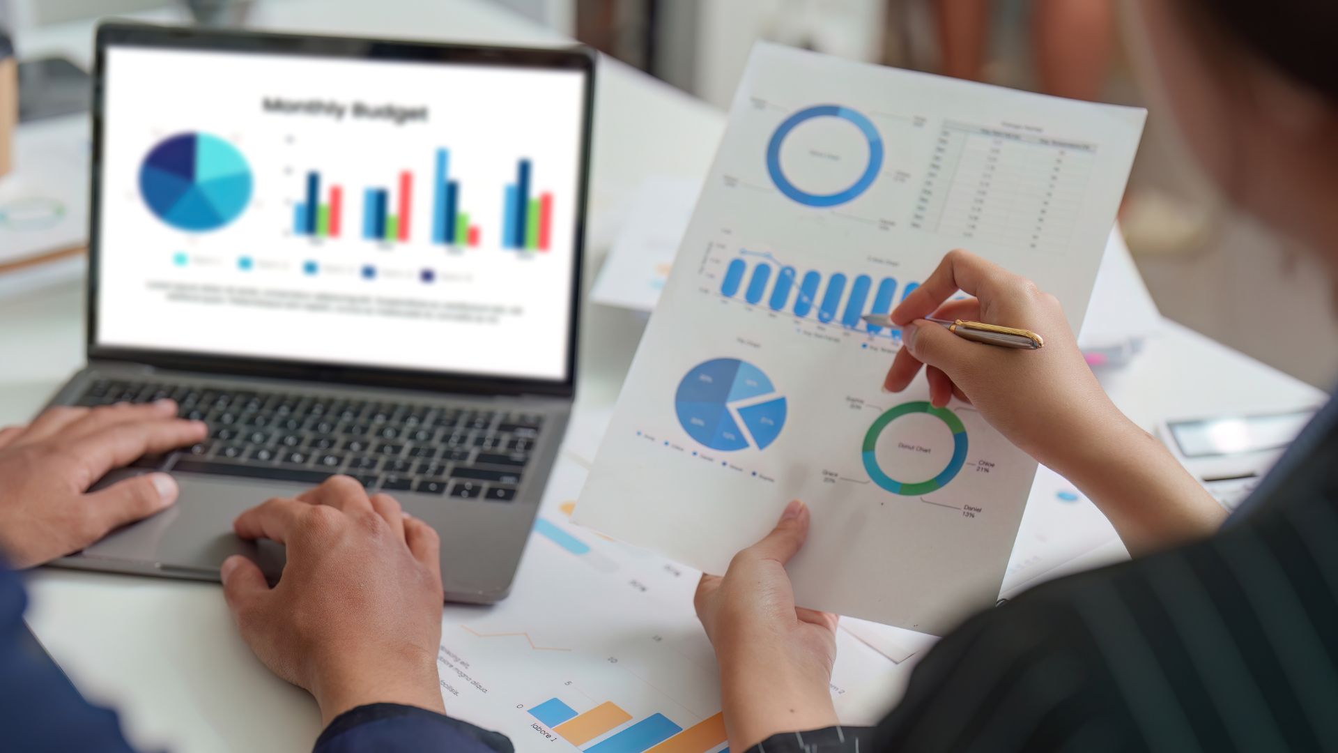 Una persona confronta i grafici di budget stampati con quelli aperti sul portatile