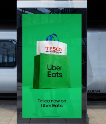Il display della campagna in stazione: la busta di Uber Eats con dentro la spesa Tesco e la scritta «Tesco now on Uber Eats»