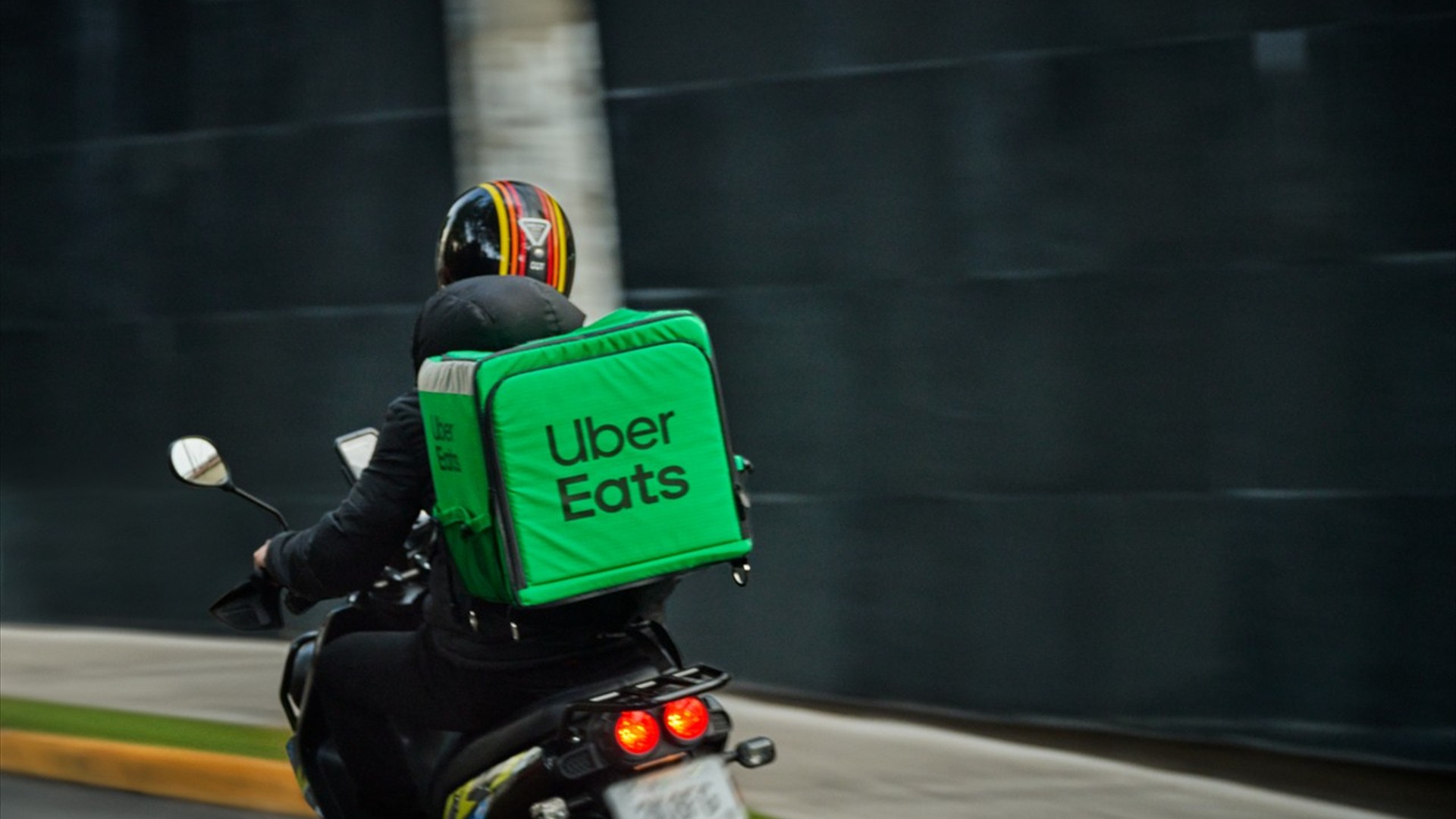 Un rider Uber Eats in sella allo scooter con lo zaino termico verde, mentre consegna per strada