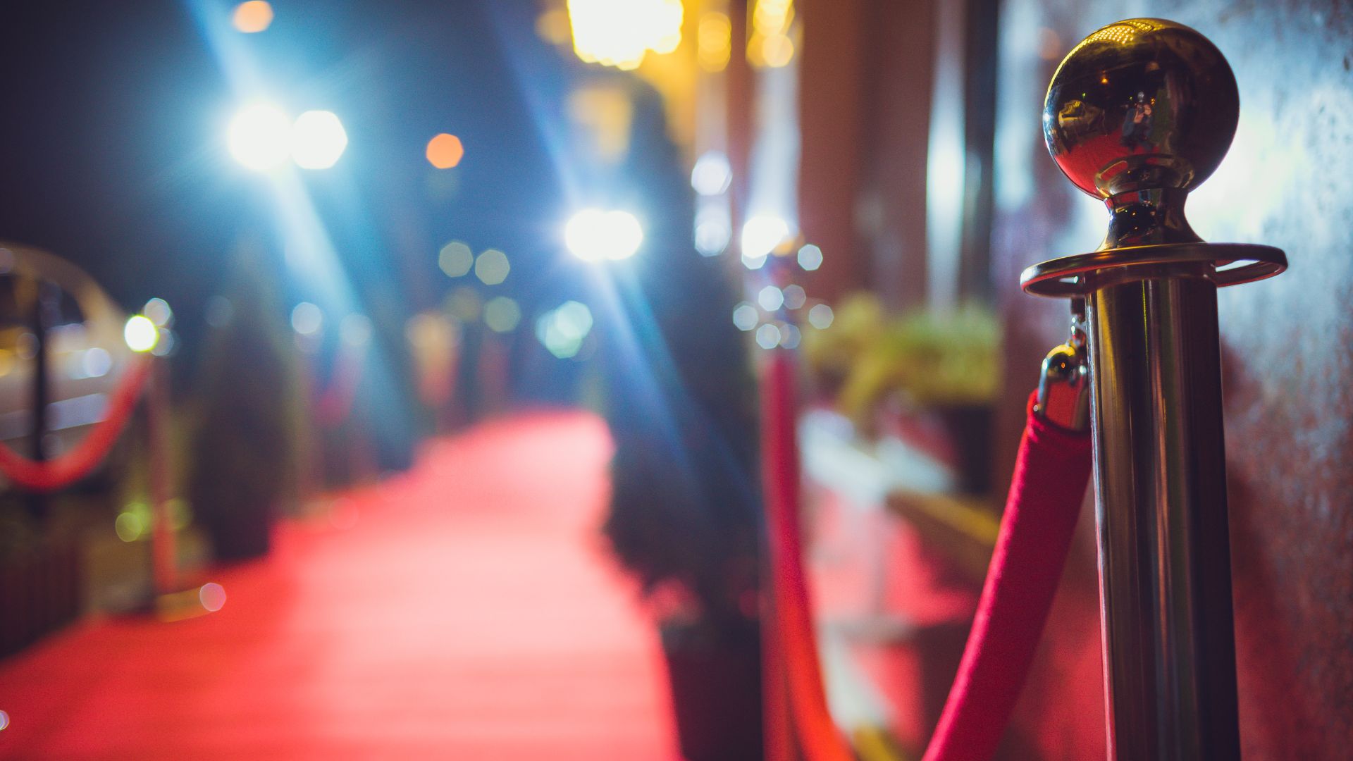 Tappeto rosso delimitato da una corda di velluto e pali in metallo, sotto i fari di un evento
