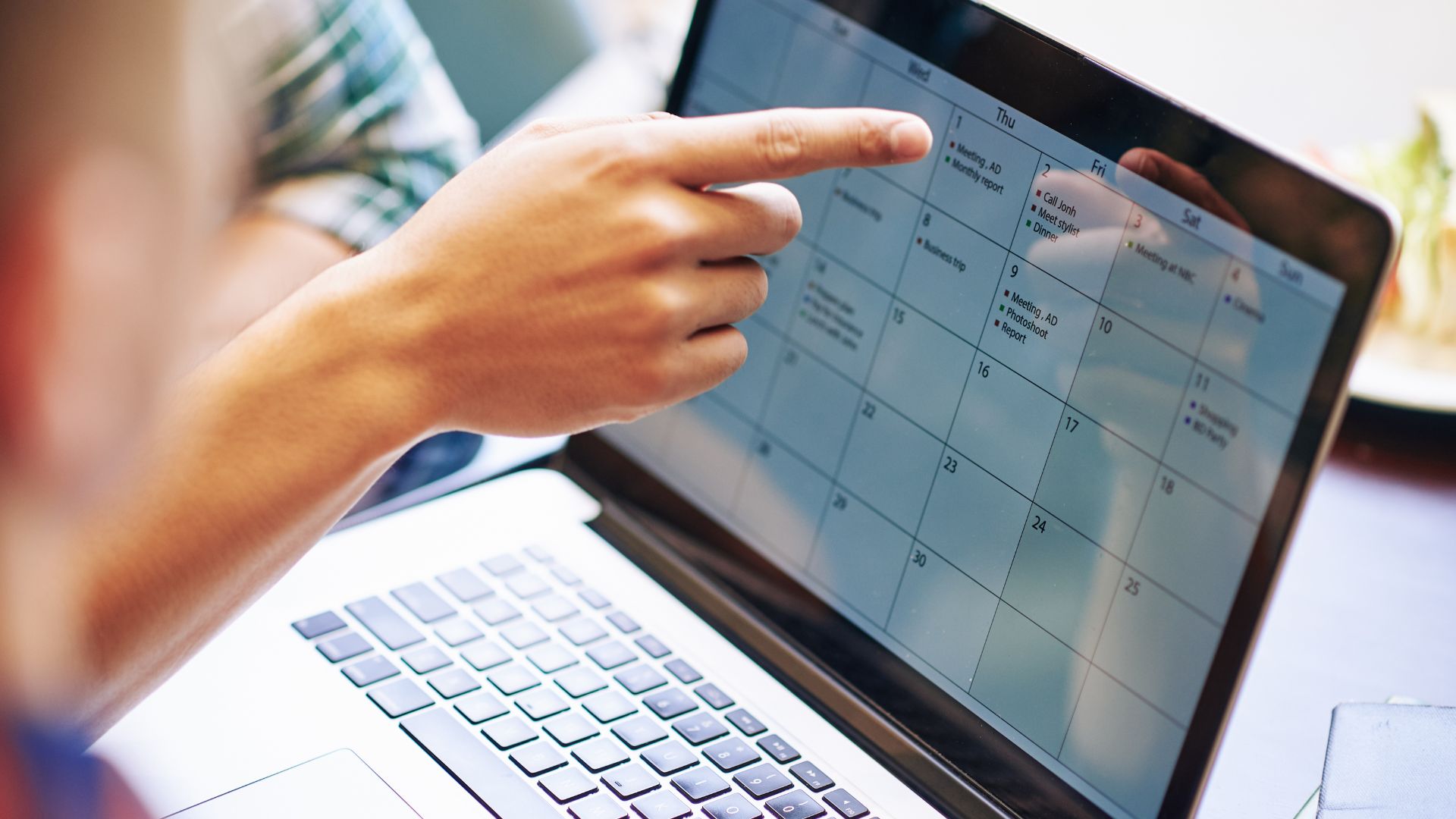 Una persona indica una data sul calendario aperto sul portatile, durante la pianificazione dei contenuti