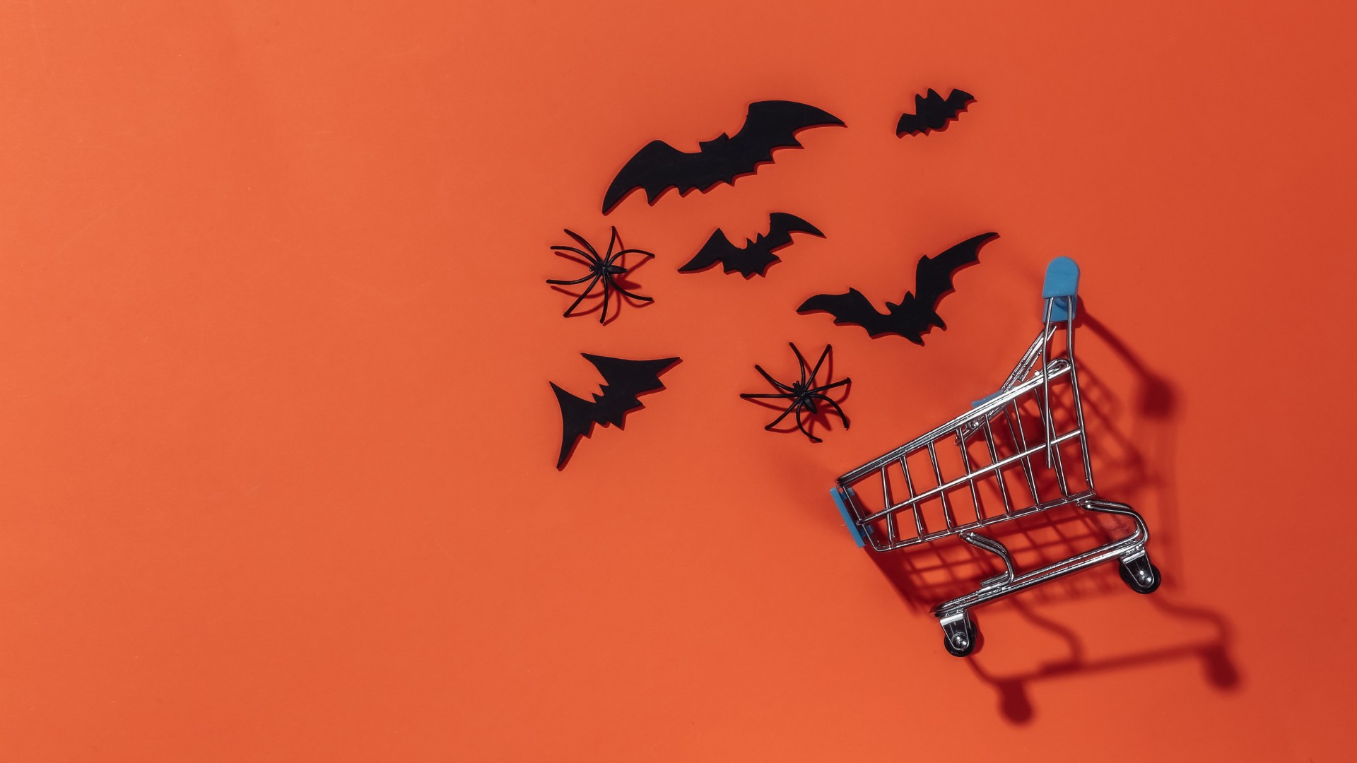 Carrello della spesa su sfondo arancione con pipistrelli e ragni di carta: la spesa al centro di una campagna di Halloween