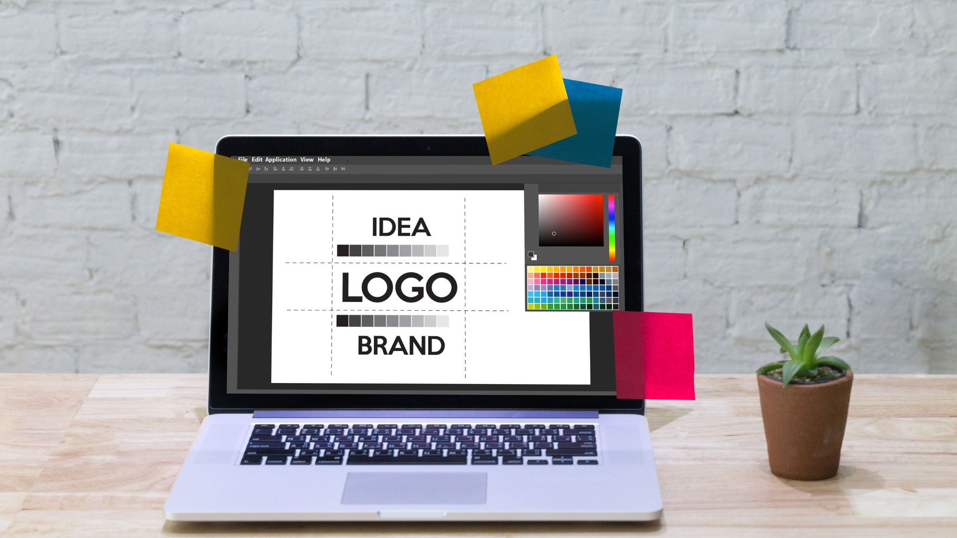 Un portatile con il software di grafica aperto e la scritta «IDEA LOGO BRAND» sul progetto, tra foglietti colorati